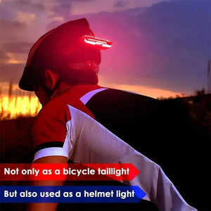 Red LED bicycle safety light mounted on the back of a cyclist's helmet at sunset.