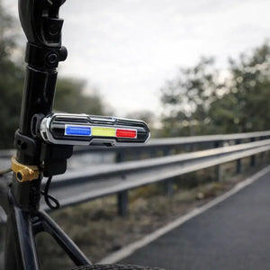 USB rechargeable bicycle tail light mounted horizontally on a seatpost beside a road.