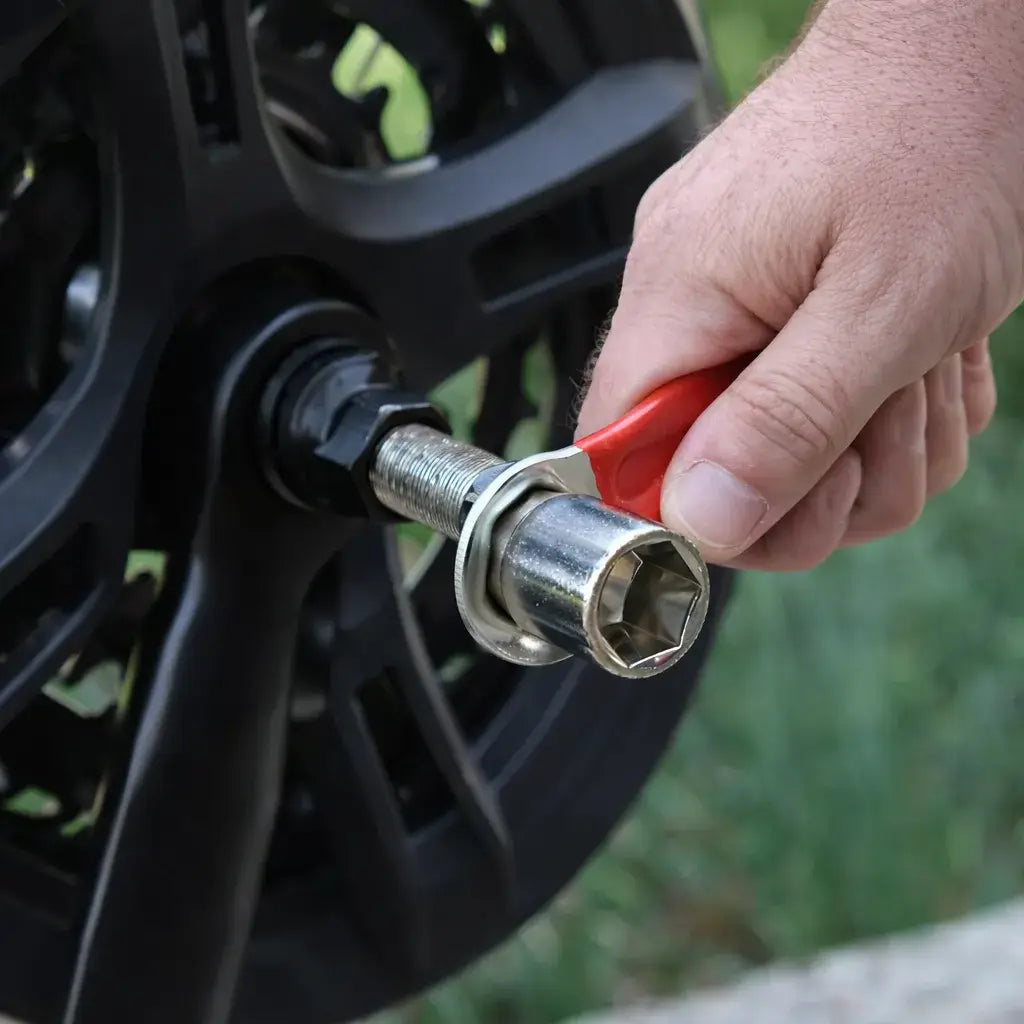 Close-up of a hand turning a red-handled wrench on a bicycle crank puller installed in a black crank arm.