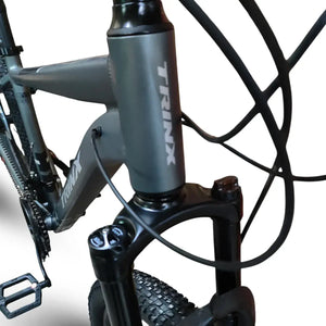 Close-up of Trinx M007 PRO mountain bike frame and front suspension fork, showing dark gray head tube with Trinx logo, brake cables, and front tire.