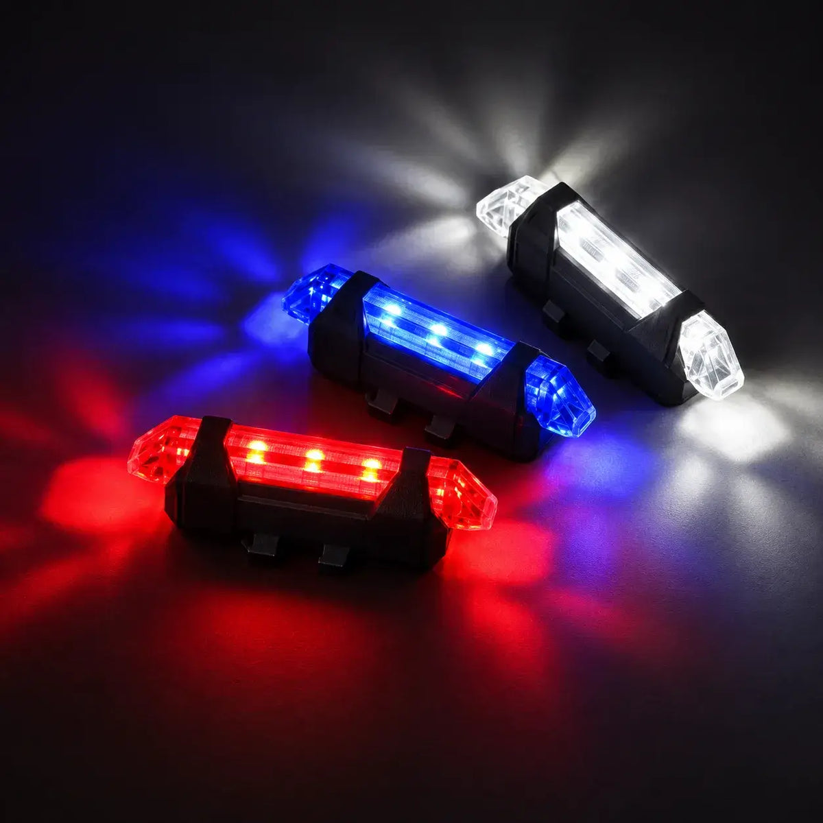 Three LED Bicycle Safety Lights Illuminated in Red, Blue, and White on a Dark Background